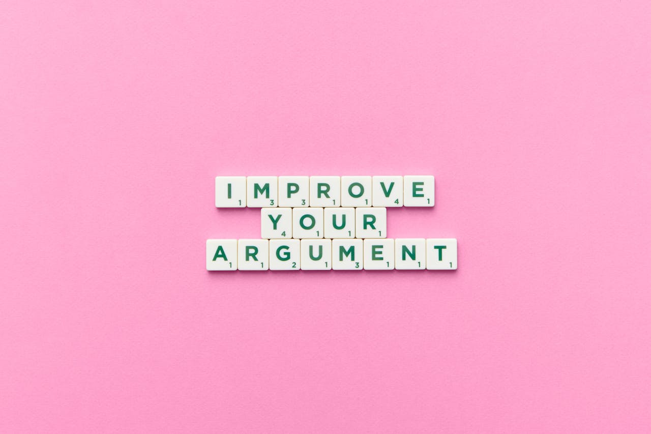 creative-01 Scrabble tile letters spelling 'Improve Your Argument' on a pink background.