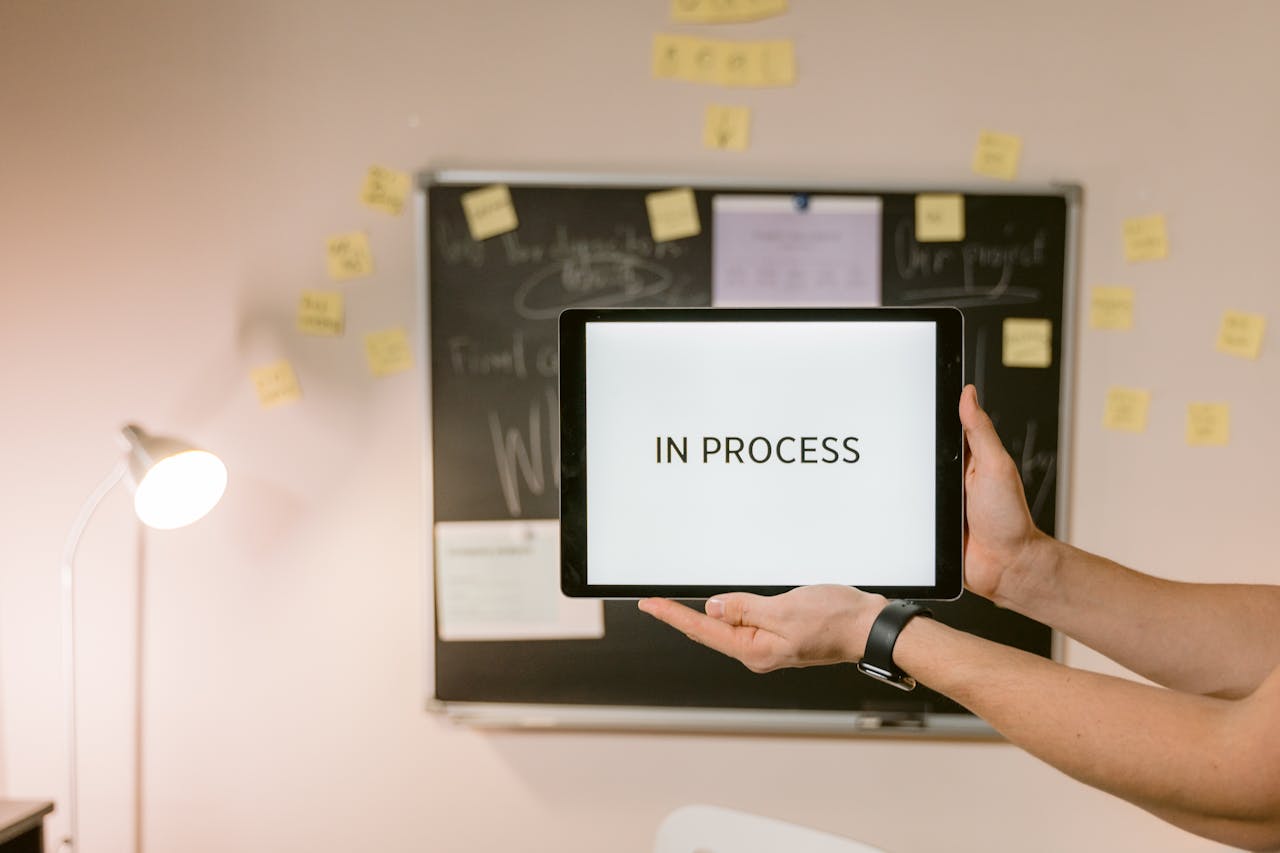 creative-03 Tablet with 'In Process' text held in an office setting, under analytical review.