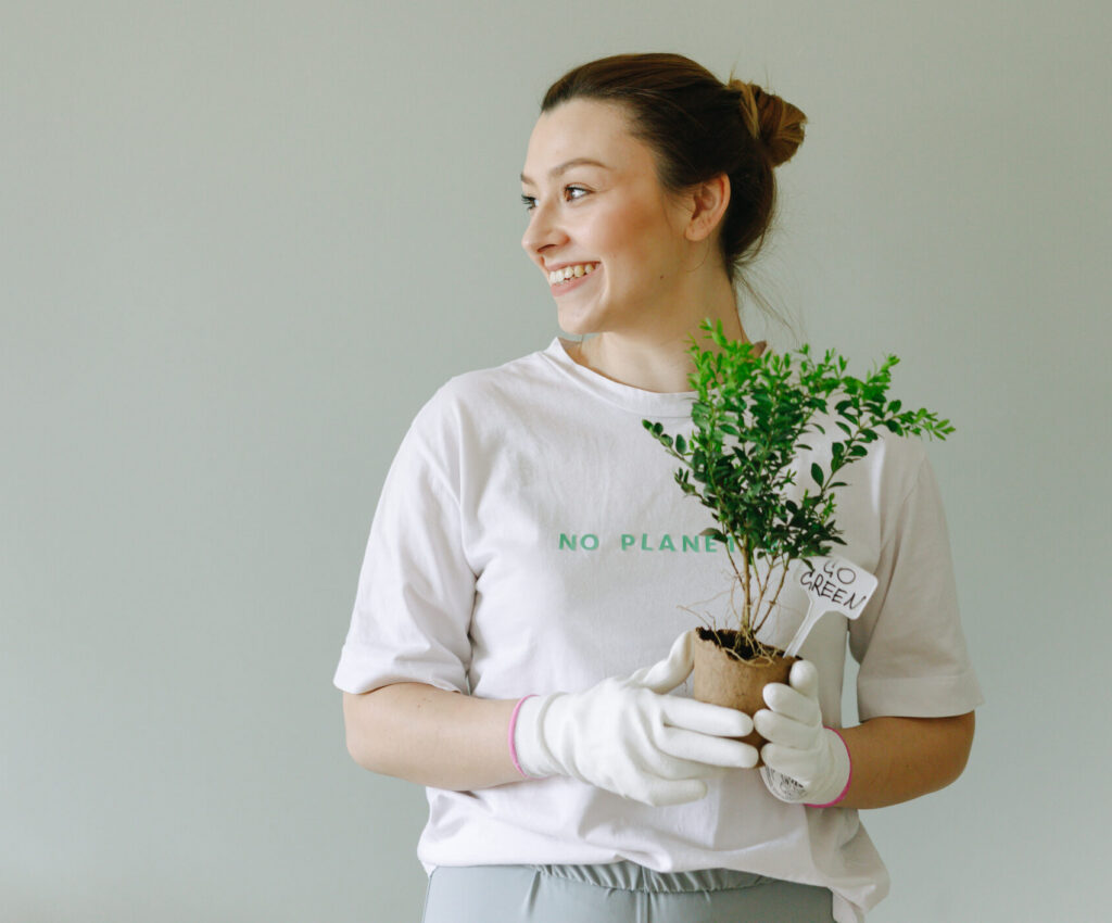 pexels-photo-7655919-7655919 A joyful woman with a potted plant stands against a plain backdrop; sustainable living concept.